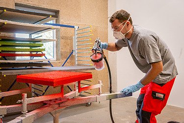 Ein Mitarbeiter der Naporo, der gerade ein Wallfield mit roter Farbe besprüht .Im Hintergrund mehrere Wallfields in verschiedenen Farben auf einem Stufenwagen